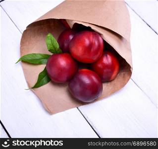 ripe red peaches in a paper bag on a white wooden table