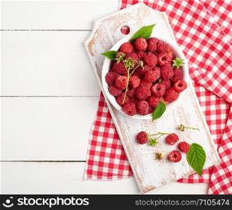 ripe red raspberries in a white wooden plate on a table of boards, textile towel, top view