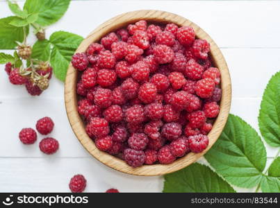 ripe red raspberries in a wooden bowl on a white table, top view