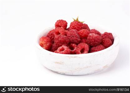 ripe red raspberries in a wooden white plate on a white background, close up