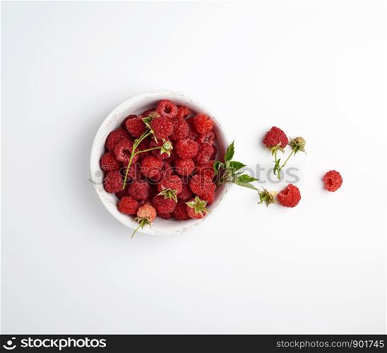 ripe red raspberries in a wooden white plate on a white background, top view