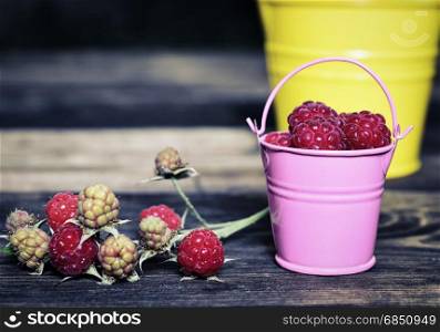 Ripe red raspberries in an iron bucket on a brown wooden background