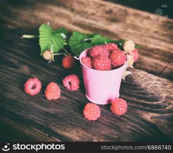 Ripe red raspberries in an iron bucket on a brown wooden background, vintage toning