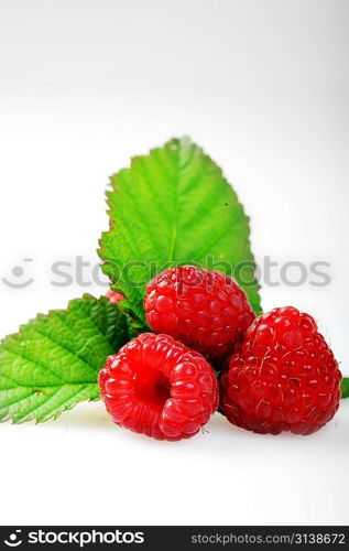 Ripe red raspberries with green leaves close up