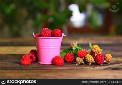 Ripe red raspberry in a pink metal bucket on a brown wooden table