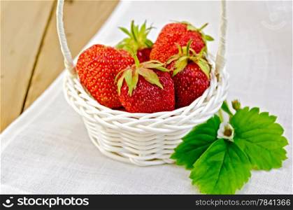 Ripe red strawberries in a white wicker basket on a napkin on the background of wooden boards