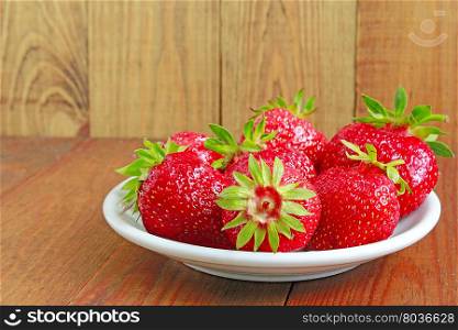 ripe red strawberries on the plate. ripe red strawberries on the white plate on the brown background