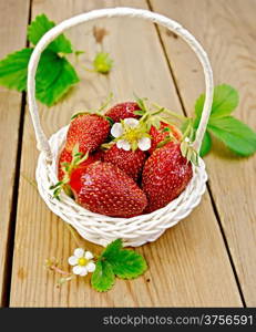 Ripe red strawberries with leaves and flowers in a white wicker basket on background wooden plank