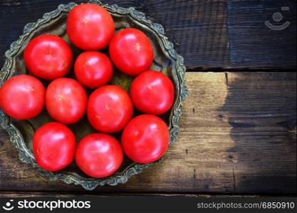 Ripe red tomatoes in an iron plate on a wooden background, top view, empty space on the right