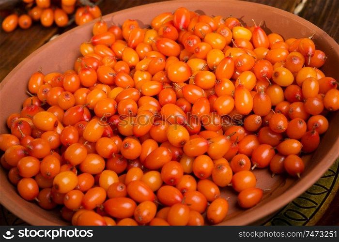 ripe sea buckthorn berries in bowl on wooden table. close up. 