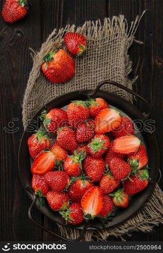Ripe strawberries in a metal dish on an old wooden background with copy space. Viewpoint from above, vertical frame. Delicious natural dessert, seasonal food