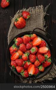 Ripe strawberries in a metal dish on an old wooden background with copy space. Viewpoint from above, vertical frame. Delicious natural dessert, seasonal food