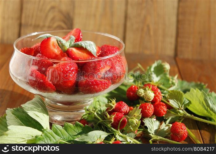 ripe strawberries in a transparent bowl and bunches with leaves. sliced ripe strawberries in a transparent bowl and strawberries bunches with leaves