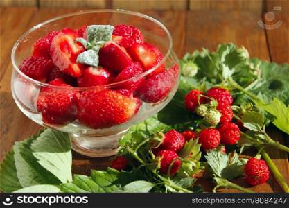 ripe strawberries in a transparent bowl and bunches with leaves. sliced ripe strawberries in a transparent bowl and strawberries bunches with leaves