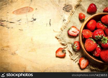 Ripe strawberries in bowl on a sack. On wooden background.. Ripe strawberries in bowl on a sack.