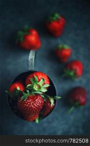 Ripe strawberries scattered around an iron mug. Ripe strawberries scattered around an iron mug. Dark photo
