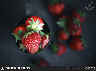 Ripe strawberries scattered around an iron mug. Ripe strawberries scattered around an iron mug. Dark photo