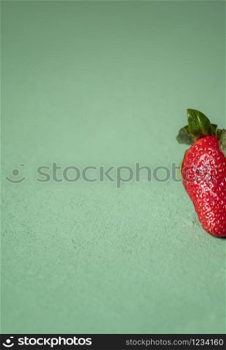 Ripe strawberry fruit on a green background. Part of one strawberry. Close-up of organic fresh strawberry. Red berries on green table. Summer fruit.