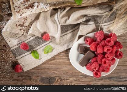 Ripe sweet raspberries and chocolate in a plate on wooden table. Close up, top view, high resolution product