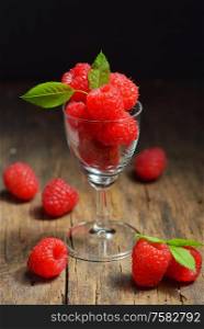 Ripe sweet raspberries in small cup on wooden table