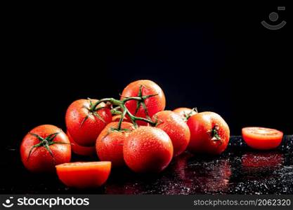Ripe tomatoes on a branch and tomato halves. On a black background. High quality photo. Ripe tomatoes on a branch and tomato halves.
