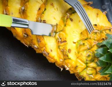 ripe vivid pineapple sliced on a black plate with knife and fork
