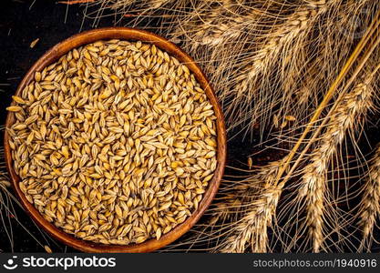 Ripe wheat grains in a wooden bowl. Top view. On a dark background. . Ripe wheat grains in a wooden bowl. Top view.