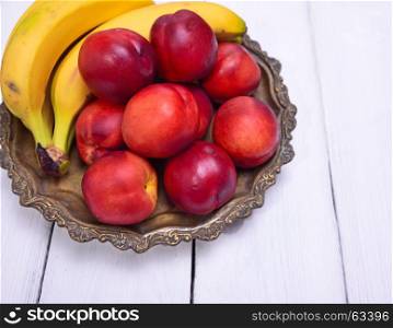 Ripe yellow bananas and red peaches on a copper plate