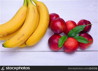 Ripe yellow bananas and red peaches on a white wooden background