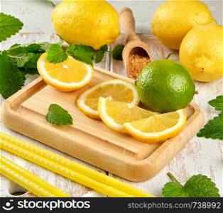 ripe yellow lemons and lime, brown sugar and a bunch of fresh mint on a white wooden board, ingredients for lemonade