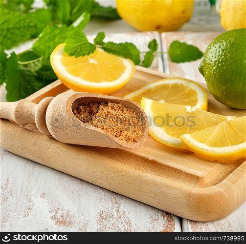 ripe yellow lemons and lime, brown sugar and a bunch of fresh mint on a white wooden board, ingredients for lemonade