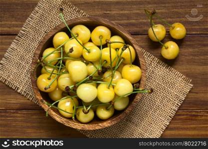 Ripe yellow or Rainier cherry in wooden bowl, photographed overhead on wood with natural light (Selective Focus, Focus on the top cherries in the bowl)