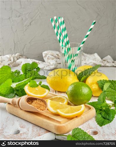 ripe yellow whole lemons and lime, brown sugar and a bunch of fresh mint on a white wooden board, ingredients for lemonade