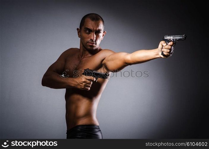 Ripped man with gun against grey background