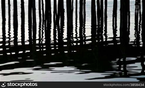Rippling lake surface and silhouettes of wooden posts making pattern of vertical lines