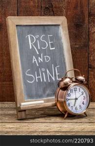 Rise and shine  sign - white chalk handwriting on a blackboard  with an alarm clock against rustic barn wood