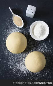 Risen or proved yeast dough balls for bread or pizza on a floured slate surface, ingredients on the side, photographed overhead with natural light (Selective Focus, Focus on the top of the dough balls)