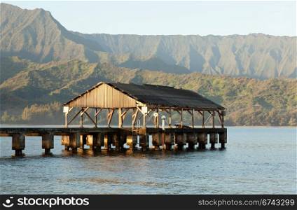 Rising sun illuminates the Hanalei pier and Na Pali mountains in Kauai
