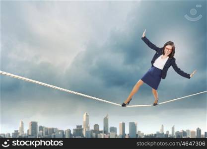 Risk in business. Young attractive businesswoman balancing on rope high in sky