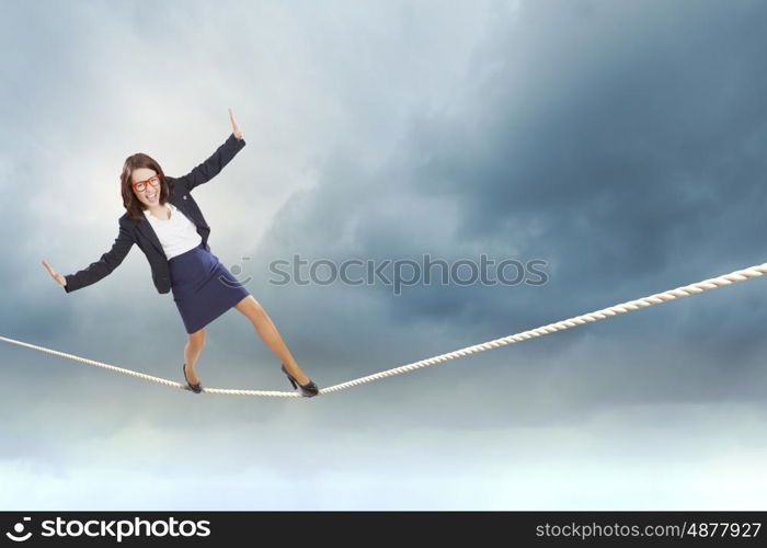 Risk in business. Young attractive businesswoman balancing on rope high in sky