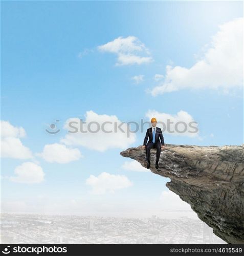Risk in business. Young businessman in helmet standing on edge of rock mountain