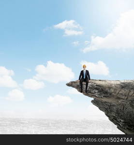 Risk in business. Young businessman in helmet standing on edge of rock mountain