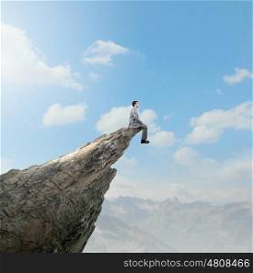 Risk in business. Young businessman sitting on edge of rock mountain