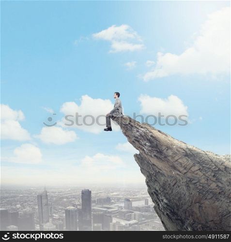 Risk in business. Young businessman sitting on edge of rock mountain