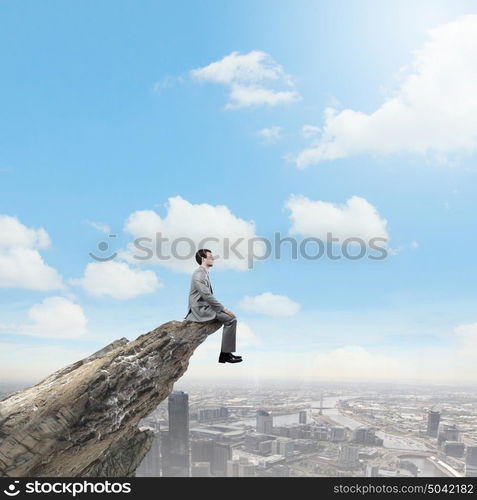 Risk in business. Young businessman sitting on edge of rock mountain