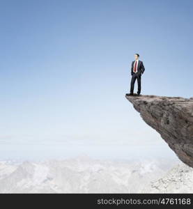 Risk in business. Young businessman standing on edge of rock mountain