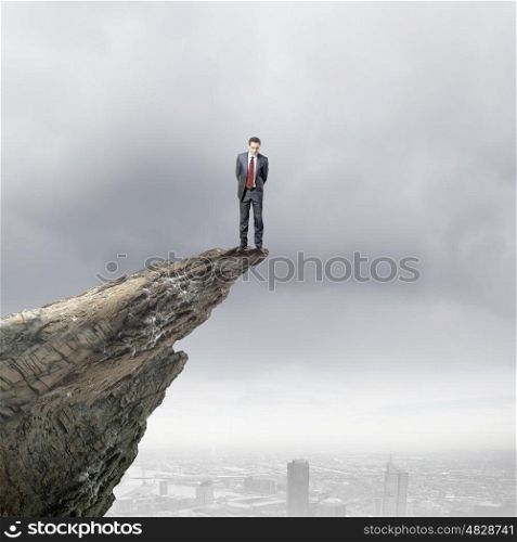 Risk in business. Young businessman standing on edge of rock mountain
