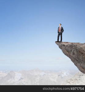 Risk in business. Young businessman standing on edge of rock mountain