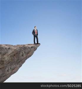 Risk in business. Young businessman standing on edge of rock mountain