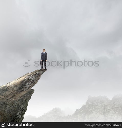 Risk in business. Young businessman standing on edge of rock mountain